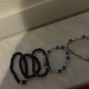 Färgglada armband med pärlor och bokstäver - Fyra armband i olika färger och stilar. Ett armband har vita pärlor med bokstäver som bildar ordet 'LOVE' och lila pärlor. De andra armbanden har pärlor i lila, blått och vitt samt elastiska band i mörklila.