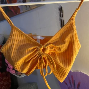 Gul ribbad croppad linnetopp med knyt - Säljer en gul ribbad croppad linnetopp med smala axelband och knyt framtill. Toppen har en v-ringad design och är perfekt för varma dagar. Använd 2 gånger bara 🩵 