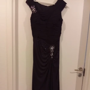 Svart långklänning med paljettdetaljer - Elegant svart långklänning med rynkad överdel och glittrande paljettdetaljer framtill. Klänningen har breda axelband och en smickrande drapering över midjan. Perfekt för festliga tillfällen.