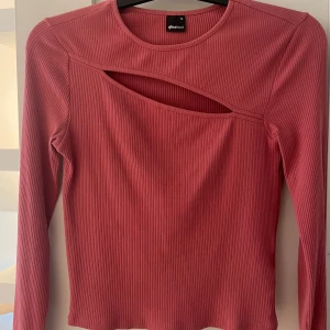 Rosa ribbad långärmad topp med cut-out från Gina Tricot - Säljer en rosa långärmad topp från Gina Tricot med ribbad struktur och snygg cut-out detalj vid bröstet. Rund halsringning och figurnära passform.