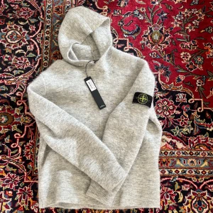 Grå hoodie från Stone Island - Säljer en grå hoodie från Stone Island med klassisk patch på ärmen. Tröjan är stickad av mohair och har en väldigt mjuk känsla, dvs. ganska varm, påminner mycket om kashmir. Den är nästintill helt oanvänd och har kvar etiketten samt äkthetsintyg. 