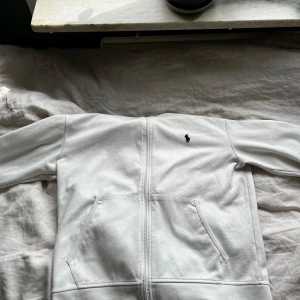 Vit zip-hoodie från Polo Ralph Lauren - Säljer min vita Ralph zip på grund av att den har blivit för liten för mig. Inga stora defekter, enbart en fläck bak på luvan som ej är synlig med luvan nere. Därav ett billigare pris då jag köpte den för 1500. Hör av dig om du skulle ha minsta fundering eller tanke!