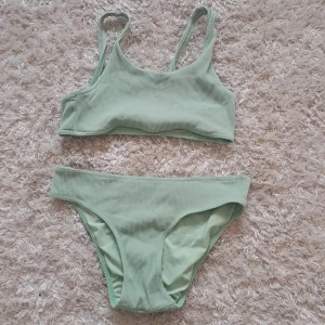 Ljusgrön ribbad bikini - Snygg ljusgrön bikini med ribbad struktur. Toppen har breda axelband och sportig passform, och bikinitrosan har en klassisk midja. Perfekt för strand eller poolhäng.