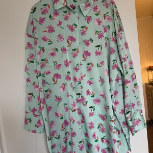 Mintgrön blommig skjorta från Zara - Säljer en mintgrön skjorta från Zara med rosa och lila blommor. Skjortan har klassisk krage, långa ärmar med manschett och knappar framtill. Perfekt för dig som gillar färg och mönster!Knappt använd,så toppenskick 