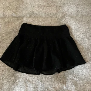 Svart prickig kjol från Gina Tricot - Supersöt svart kjol från Gina Tricot med små diskreta prickar i tyget. Kjolen har en kort modell och ett lätt, luftigt material. Tyvärr kom den bara till användning under nyår 😇 