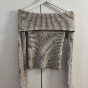 Grå ribbad offshoulder stickad tröja från H&M - Säljer en snygg grå stickad tröja från H&M i ribbat material. Tröjan har offshoulder-design med bred krage och långa ärmar. Perfekt för dig som vill ha en trendig och mysig look.