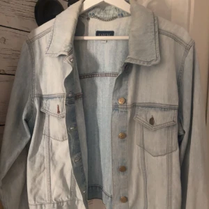 Ljusblå jeansjacka  - Säljer en klassisk ljusblå jeansjacka med bröstfickor och metallknappar. Jackan har lång ärm och en rak passform. Den är i storlek L men passar mig perfekt som har storlek s/m eftersom den är väldigt liten i storlek