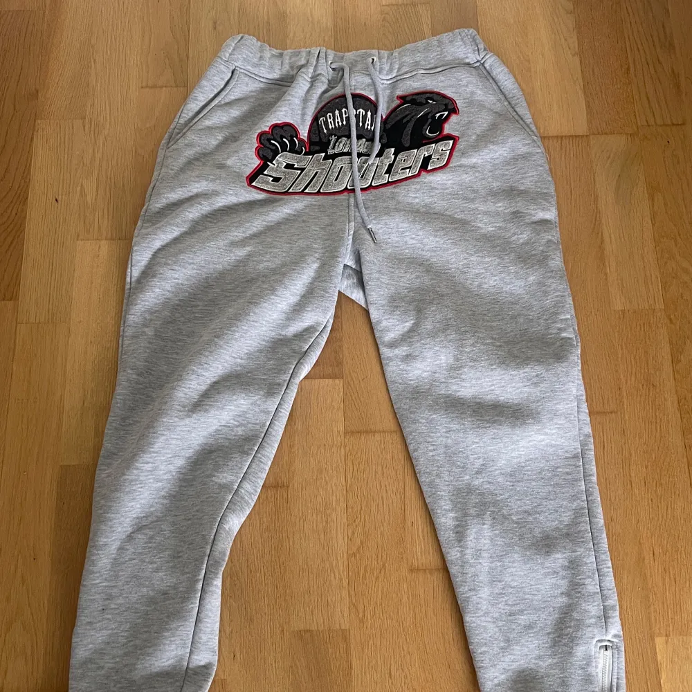 Säljer en grå tracksuit från Trapstar London med stor broderad logga och texten 'Shooter' på bröstet. 🤩Helt ny och oanvänd, storlek M😁. Ny pris runt 2499-3499 kr. Pris kan diskuteras. Kan även bytas.. Neuletakit & Villapaidat.
