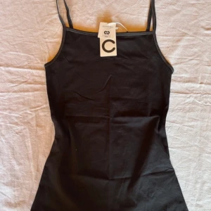 Svart linnetopp med smala axelband - Snygg svart linnetopp med smala axelband och rak halsringning. Perfekt att styla till olika outfits och passar året runt. Enkel och stilren design.