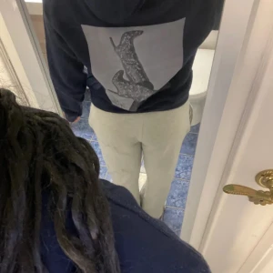 Svart hoodie med tryck - Säljer en svart hoodie med stor ficka framtill och ett stort grafiskt tryck på ryggen. Perfekt för en avslappnad stil och enkel att matcha med andra plagg.