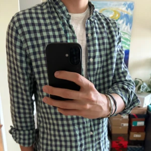 Grönblå rutig linneskjorta - Säljer en grönblå rutig skjorta med knappar och klassisk krage. Skjortan har lång ärm och normal passform, perfekt att bära öppen över en t-shirt eller knäppt. Snygg och enkel att styla till jeans eller chinos.