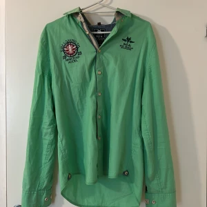 Grön skjorta från NZA - Snygg grön skjorta från NZA med broderade detaljer på bröstet. Skjortan har klassisk krage, knäppning framtill och långa ärmar. Perfekt för dig som vill sticka ut lite extra med en färgglad stil. Skjortan är i storlek S, köp gärna via köp nu. Hitta mer plagg i profilen.