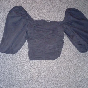 Svart topp med puffärmar - Trendig svart topp med stora puffärmar och fyrkantig ringning. Toppen är tight i passformen och har en croppad längd. Perfekt för att skapa en statement-look.