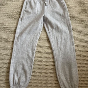 Grå mjukisbyxor från Primark - Säljer ett par ljusgrå mjukisbyxor från Primark i storlek XS. Byxorna har resår i midjan med dragsko och resår vid bensluten. Perfekta för en avslappnad stil och superbekväma att ha på sig.