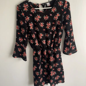 Svart blommig klänning från  - Säljer en svart kortklänning från h&m med rött och vitt blommönster. Klänningen har trekvartsärm, rund halsringning och resår i midjan för en smickrande passform. Perfekt för vår och sommar! Säljer för 50kr!, pris går att diskutera😻❤️ så fin klänning verkligen, tänker att den blir perfekt nu till midsommar🥹❤️