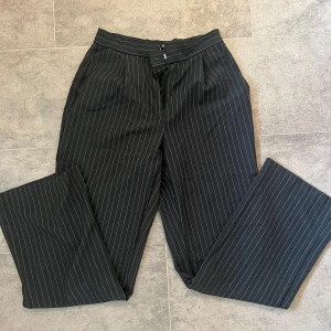 Svarta kostymbyxor med vita ränder - Säljer ett par svarta kostymbyxor med tunna vita ränder. Byxorna har hög midja, raka ben. Säljer eftersom dom blivit lite för små och korta för mig.