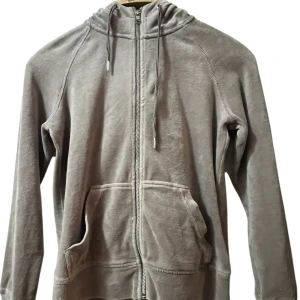 Beige hoodie med dragkedja - Mysig beige hoodie med dragkedja framtill och huva med dragsko. Tröjan har långa ärmar och en stor ficka framtill. Perfekt för en avslappnad stil.