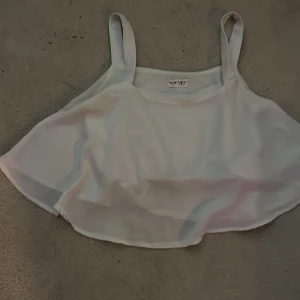 Vit croppad linnetopp - Säljer en vit croppad linnetopp med breda axelband och lös passform. Toppen har dubbla lager tyg och resår i ryggen för extra komfort. Perfekt för varma dagar och enkel att matcha med olika outfits.