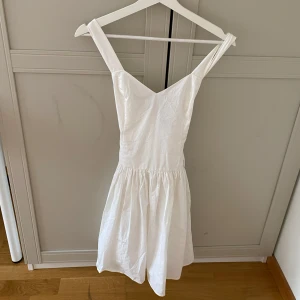 Vit kläning med knyt i ryggen - Säljer en söt vit klänning perfekt för en sommar avslutning eller studentfest. Klänningen har en markerad midja och en lätt utställd kjol. Baksidan har en fin knytdetalj och dragkedja. Perfekt för sommarens alla tillfällen!