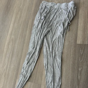 Grå mjukisbyxor med dragsko - Säljer ett par grå mjukisbyxor med resår i midjan och dragsko för justerbar passform. Byxorna har en avslappnad och loose passform, perfekta för en chill dag hemma eller till träning. Lite strynkliga på bilden.