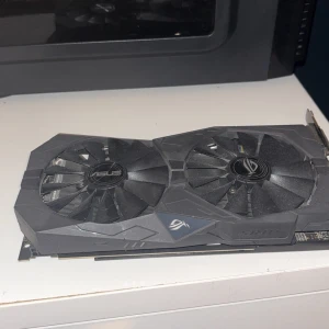 RX570 4gb  ASUS ROG Strix grafikkort - Säljer ett ASUS ROG Strix grafikkort med dubbla stora fläktar och svart kylare. Kortet har en robust design med tydliga ROG-loggor och passar för gaming och krävande grafikapplikationer. PCIe-anslutning och flera utgångar på baksidan. ANVÄND 1 år 