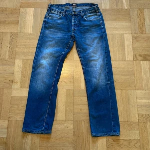 Blå jeans från Lee - Klassiska blå jeans från Lee med raka ben och normal passform. Jeansen har fem fickor, dragkedja och knapp med Lee-logga. Snygga kontrastsömmar och diskret Lee-märke bak i midjan.