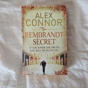 The Rembrandt Secret - Spännande thrillerbok av Alex Connor. 'The Rembrandt Secret' handlar om en seriemördare och en uråldrig konspiration kopplad till konstvärlden. Perfekt för dig som gillar mysterier, konst och mörka hemligheter. Omslaget har antika och dramatiska inslag med siluett av en person i en pelargång.