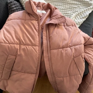Rosa pufferjacka från H&M - Säljer en rosa pufferjacka från H&M i storlek M. Jackan har dragkedja framtill, hög krage och två fickor på sidorna. Perfekt för kyligare dagar och enkel att matcha med olika outfits.