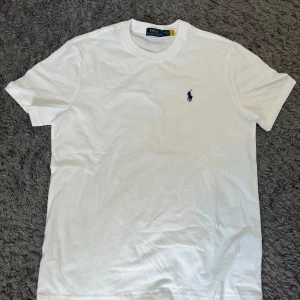 Vit t-shirt från Ralph Lauren - Storlek M. Vit t-shirt från Ralph Lauren. Liten broderad logga i svart på bröstet. Tillverkad i mjuk bomull. Stilren design. Jätte bra material och kvalite. Nästan helt oanvänd och helt ren. PRISET KAN DISKUTERAS.