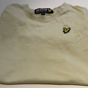Ljusgul t-shirt från Lyle & Scott - Snygg ljusgul t-shirt från Lyle & Scott med klassisk rund hals och broderad gul logga på bröstet. Har använt den sparsamt 🤩