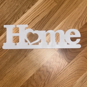 Vit dekoration med texten 'Home' - Säljer en vit dekorationsskylt i trä med texten 'Home' där O:et är utformat som ett hjärta. Perfekt som inredningsdetalj för att skapa en mysig känsla i hemmet. Skylten är platt och står stadigt på en hylla eller ett bord.