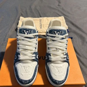 Louis Vuitton LV trainer Storlek 43 - Säljer ett par exklusiva Louis Vuitton sneakers i vitt och blått med tydliga LV-loggor på både plös och häl. Skorna har snörning, rund tå och är tillverkade i en mix av skinn och textil med mönstrade blå detaljer.