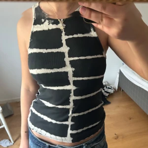 Svart och vit ribbad linnetopp - Säljer en svart ribbad linnetopp med vita oregelbundna ränder och synliga sömmar. Toppen har ärmlös design och rund halsringning. Perfekt för en trendig och avslappnad stil.