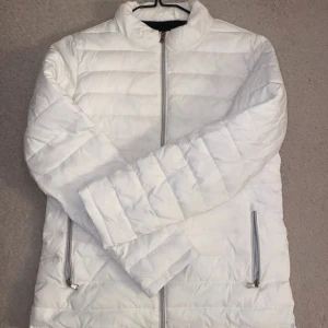 Vit pufferjacka från Long Island - Säljer en vit pufferjacka från Long Island med dragkedja framtill och två sidofickor med dragkedja. Jackan har lång ärm och en enkel, stilren design som passar perfekt till kyligare dagar.