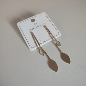 Guld örhängen  - Säljer ett par oanvända eleganta guldiga örhängen från Dekorazia, köpta i Spanien. Örhängena har två kedjor med glasdiamanter och små bladformade hängen i guld, vilket ger en stilren och trendig look. Perfekta för att lyfta din outfit!