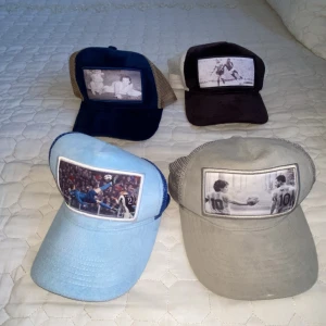 Fyra kepsar med fotomotiv - Fyra kepsar i olika färger med unika fotomotiv framtill. En ljusblå keps med fotbollsmotiv, en grå keps med svartvitt fotomotiv, en mörkblå och beige keps samt en svart och vit keps, båda med svartvita bilder. Alla har klassisk kepsform och nät baktill.