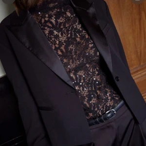 Svart spetsblus med paljetter - Säljer en svart långärmad spetsblus med paljetter. Blusen har hög hals, transparent spetsmaterial och volangdetaljer vid ärmsluten. 