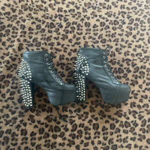 Svarta platåboots med nitar från Jeffrey Campbell - Säljer ett par svarta boots med hög platå och klack från Jeffrey Campbell. Skorna har snörning framtill och är dekorerade med silvriga nitar längs hälen och klacken. Perfekta för dig som vill sticka ut med din stil.