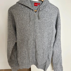 Grå hoodie med dragkedja från RYVLS - Mysig grå hoodie från RYVLS i mjukt material med dragkedja framtill och huva. Perfekt för en avslappnad stil. Tillverkad i en blandning av polyester, nylon och ull.