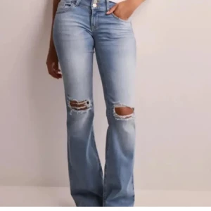 Nelly Ljusblå bootcut jeans med hål - Snygga ljusblå jeans med bootcut passform och slitna hål på båda knäna. Säljs pågrund av att de är för små. Jeansen är andvända men inget man ser på de, höra av er om ni vill ha fler bilder❤️