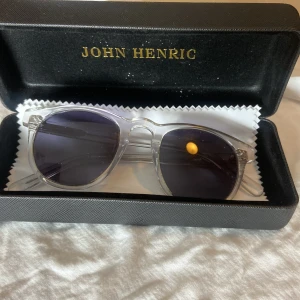 solglasögon från John Henric - Snygga solglasögon med transparent båge och mörka linser från John Henric. Klassisk form med stilren design, levereras i originalfodral med putsduk. Perfekt accessoar för soliga dagar.
