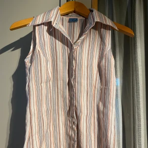 Randig ärmlös skjorta från Dana Collection - Säljer en ärmlös skjorta från Dana Collection i storlek S/M. Skjortan har ett randigt mönster i vitt, rosa och svart med klassisk krage och knäppning framtill. Perfekt för varma dagar och enkel att styla till olika outfits.💕