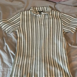 Randig stickad pikétröja - Säljer en stickad pikétröja med korta ärmar och krage. Tröjan har ett randigt mönster i vitt och grönt,  Perfekt för en avslappnad men stilren look. Storleken på tröjan är S men skulle säga att den sitter som M. Vid intresse eller frågor är det bara att skriva.