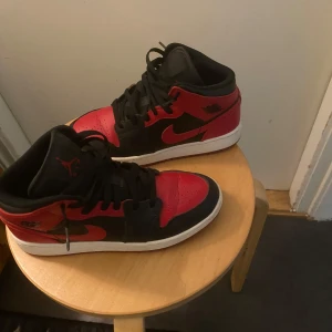 Nike Air Jordans i rött och svart - Säljer ett par klassiska Nike Air Jordans med svart och rött läder, vita sulor och svarta skosnören. Ikonisk design med högt skaft och tydlig Jumpman-logga på plösen. Perfekta för dig som gillar streetwear och sneakers med attityd.