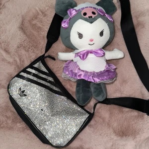 Glittrig axelväska från Adidas - Säljer en snygg axelväska från Adidas med glittriga stenar och svarta detaljer. Väskan har ett klassiskt Adidas-märke och justerbar axelrem. Perfekt för dig som vill sticka ut med en sportig men glamorös look 💅💅 (OBS några av diameterna saknas som du kan se på bilden)