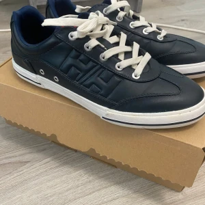 MörklBlåa sneakers från Helly Hansen - Säljer ett par svarta Helly Hansen sneakers med vit sula och vita snören. Skorna har HH-logga på sidan och klassisk rund tå. Ovandelen är i skinn och insidan är fodrad i mörkblått tyg. Perfekta för en stilren vardagslook. Skick 10/10
