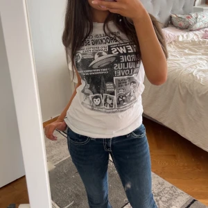 Vit t-shirt med svart tryck från Paul Frank - Säljer en vit t-shirt från Paul Frank med stort svart tryck framtill i tidningsstil. T-shirten har rund halsringning och korta ärmar. Perfekt för dig som gillar grafiska prints och streetstyle.