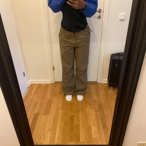 Olivgröna parachute pants från BERSHKA  - Säljer ett par olivgröna parachute pants från Bekka med dragsko i midjan och vida ben. Byxorna har fickor på sidorna och är tillverkade i bomull. Perfekta för en avslappnad stil - pris kan diskuteras