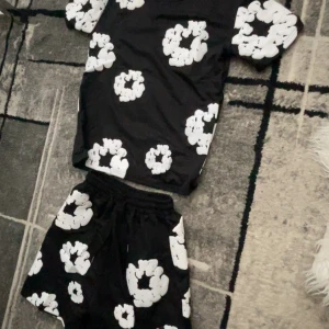 Helt ny Denim Tears  set /Svarta shorts med vit blomliknande print i storlek S - O används DENIM TEARS svart set med vita blomm print /style. Perfekta för en trendig och bekväm stil.