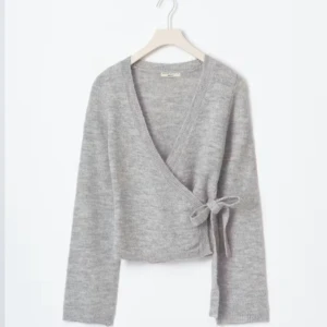 Grå omlottkofta från Gina tricot M - Säljer en stilren grå omlottkofta från Gina tricot. Koftan har en knytning i sidan och långa ärmar. Perfekt för en mysig och trendig look. Passar bra till både jeans och kjol.